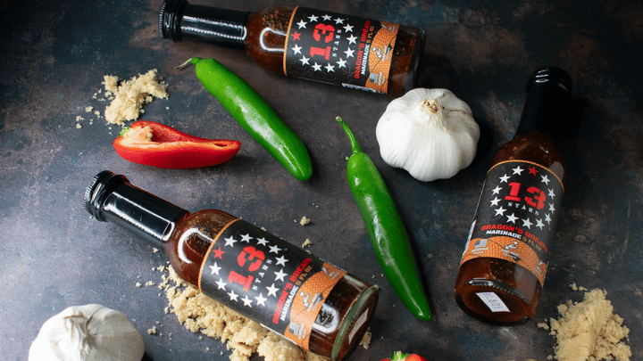 3 Bottles of 13 Stars Dragon's Breath Everything sauce on a table with its raw ingredients around it
