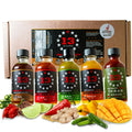 Five bottles of 13 Stars Hot Sauce arranged in front of a cardboard gift box, with colorful ingredients including red chilies, lime, ginger, mango, and green chilies placed in front. A Scoville Winner badge is visible on the box.
