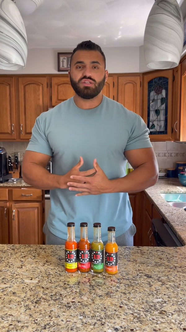 Man standing in a kitchen with six hot sauce bottles on the counter
