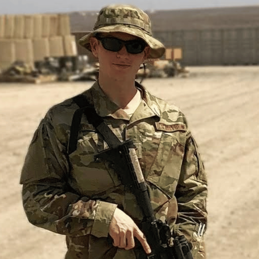 Sean in military uniform holding a rifle in an outdoor setting